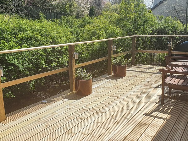 A wooden deck with a railing, potted plants, and a bench.