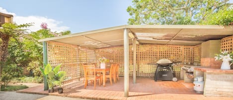 A covered outdoor patio with a grill, seating area, and potted plants.