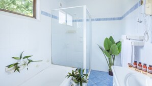 Un baño con ducha, lavabo e inodoro. Hay plantas y artículos de aseo sobre el mostrador.