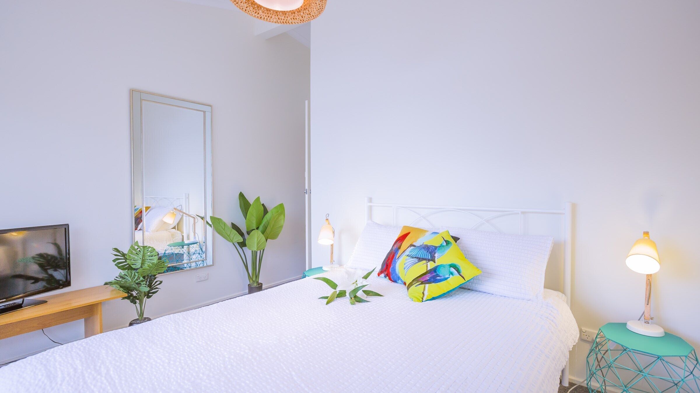 A neatly arranged bedroom with a bed, bedside tables, a TV, and a mirror.