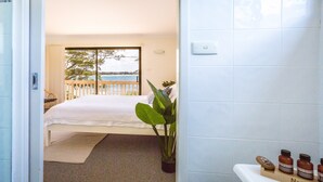 Un dormitorio con cama, una planta en maceta y vista al mar desde una puerta balcón.