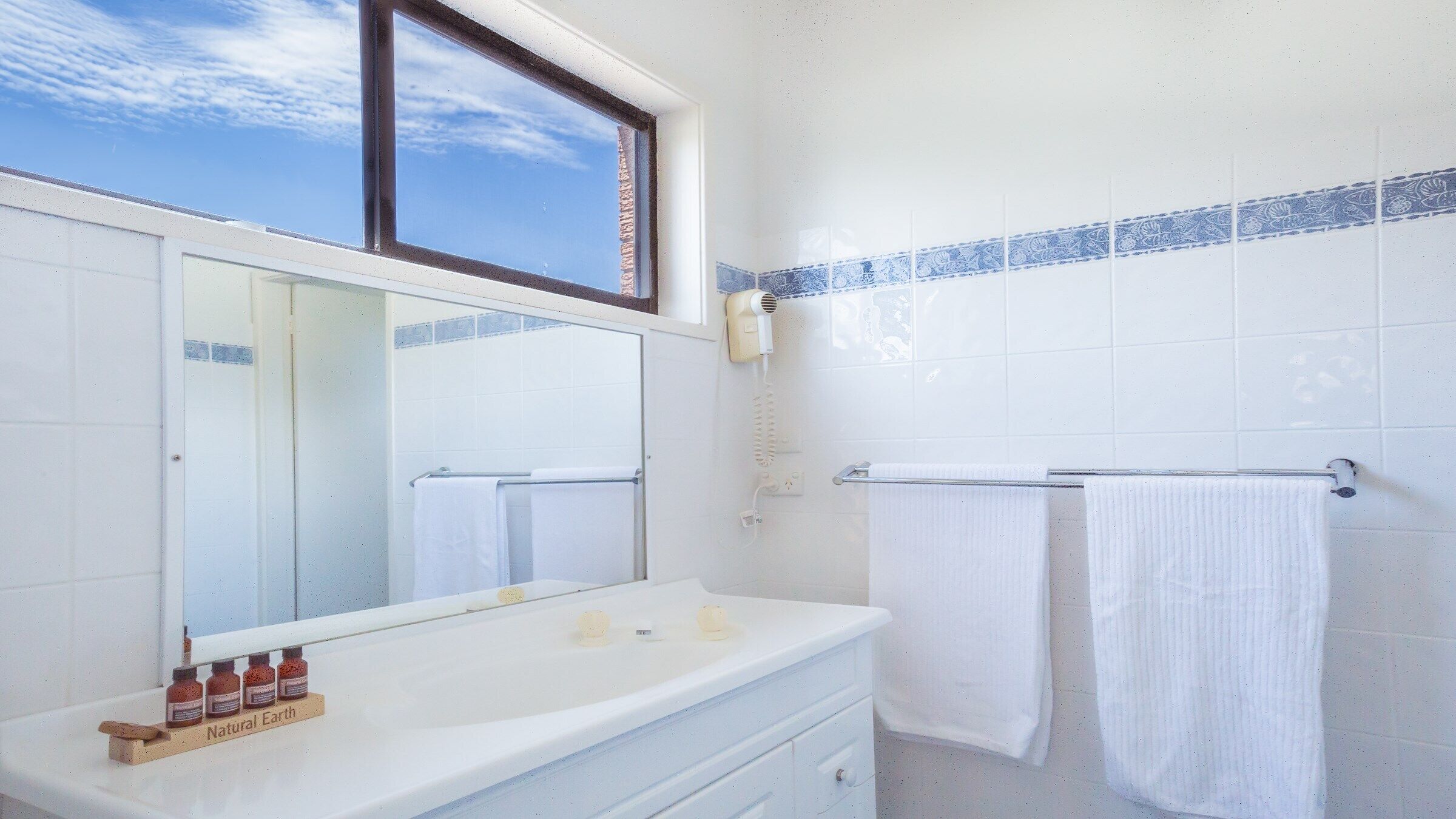 Une salle de bain avec un grand miroir, un lavabo équipé de produits de toilette et deux serviettes suspendues à un porte-serviettes.