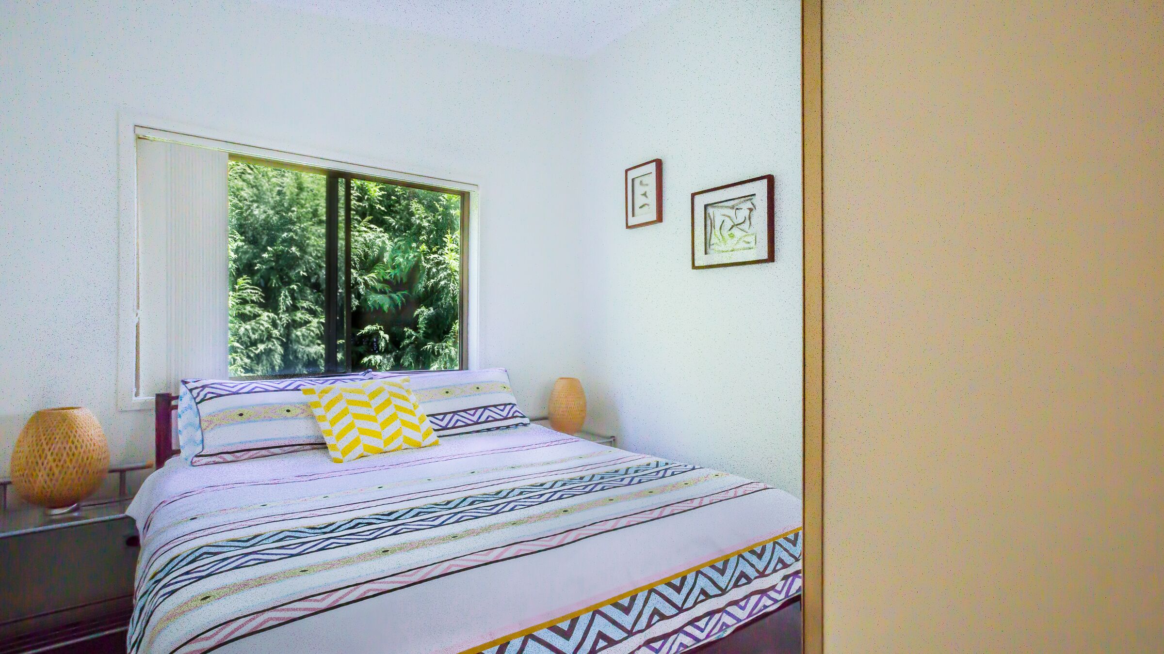 Camera da letto con un letto, due cuscini, una finestra e due quadri appesi al muro.