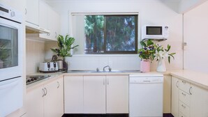 Cocina compacta con gabinetes blancos, una ventana, un microondas, un tostador y dos plantas en macetas.