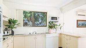 A kitchen with white cabinets, a window with a view of trees, a microwave, and a dishwashing machine.