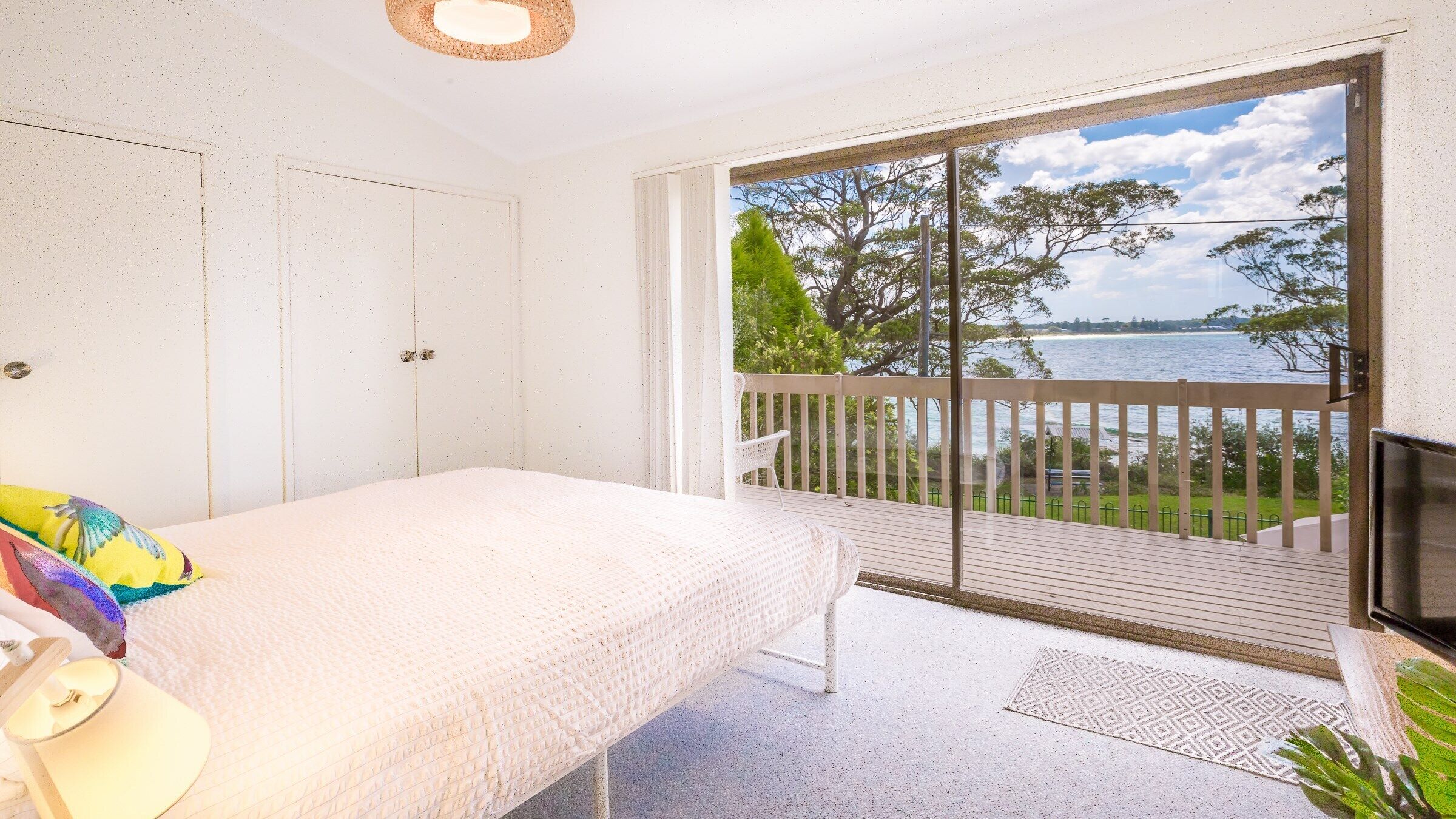 A bedroom with a bed, a TV, and a balcony with a view of the sea.