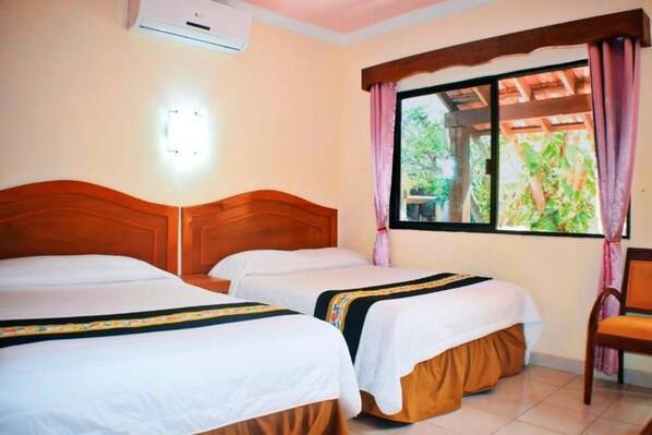 A hotel room with two beds, a wooden headboard, a window with curtains, and a chair.