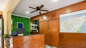 Een receptiegedeelte met een houten receptiebalie, een plafondventilator, een kaart aan de muur en een betegelde vloer.