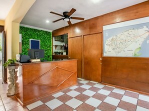 A reception area with a wooden reception desk, a ceiling fan, a map on the wall, and a tiled floor. - Hotel Hacienda Sanchez (Valladolid)