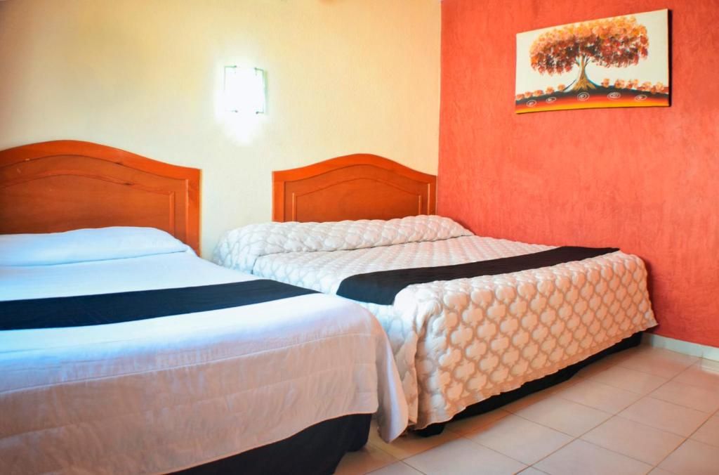 A hotel room with two beds, a red accent wall, and a painting of a tree.