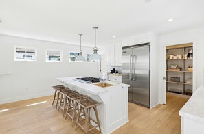 A modern kitchen with a central island, bar stools, stainless steel appliances, and pendant lighting.