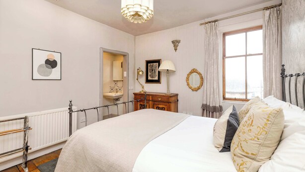 A bedroom with a large bed, a dresser, a mirror, a window with curtains, and a radiator. - Stunning Apartment in Royal Mile (Edinburgh)