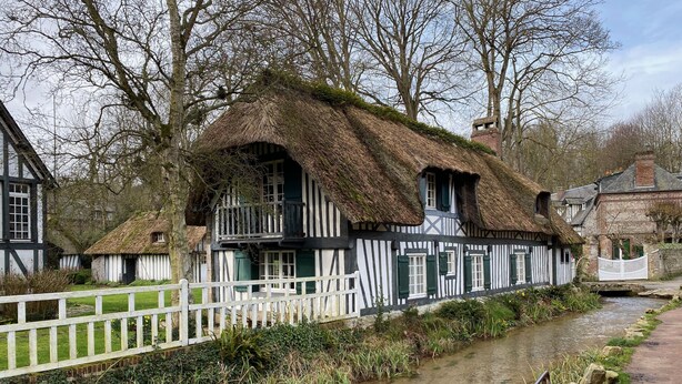 A traditional half-timbered house with a thatched roof, a white fence, and a narrow water channel in front. - Charming fisherman's house near the beach and the village center (Veules-les-Roses)