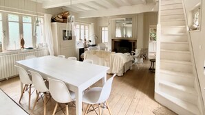 A spacious room with a large white table and chairs, a fireplace, and a staircase. - Charming fisherman's house near the beach and the village center (Veules-les-Roses)