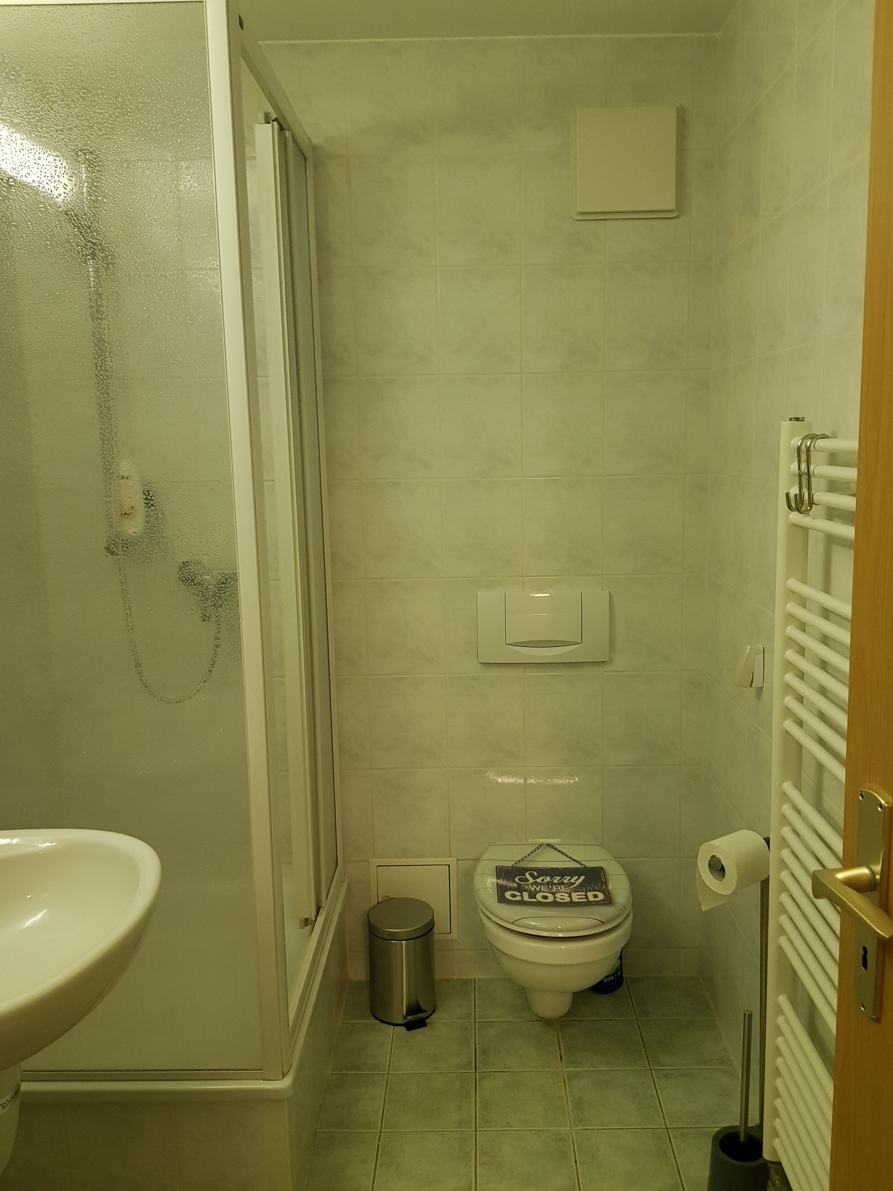 Ein kleines Badezimmer mit Toilette, Mülleimer, Dusche und Waschbecken.