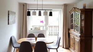 A dining area with a round table, four chairs, a chandelier, and a cabinet. - Holidays directly in the spa town of Oberwiesenthal in a modern, cozy 3-room apartment (Kurort Oberwiesenthal)