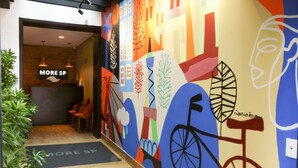 A hallway with a colorful mural, a reception area with a 'More SP' sign, and a seating area with red chairs. - Hostel More SP (São Paulo)