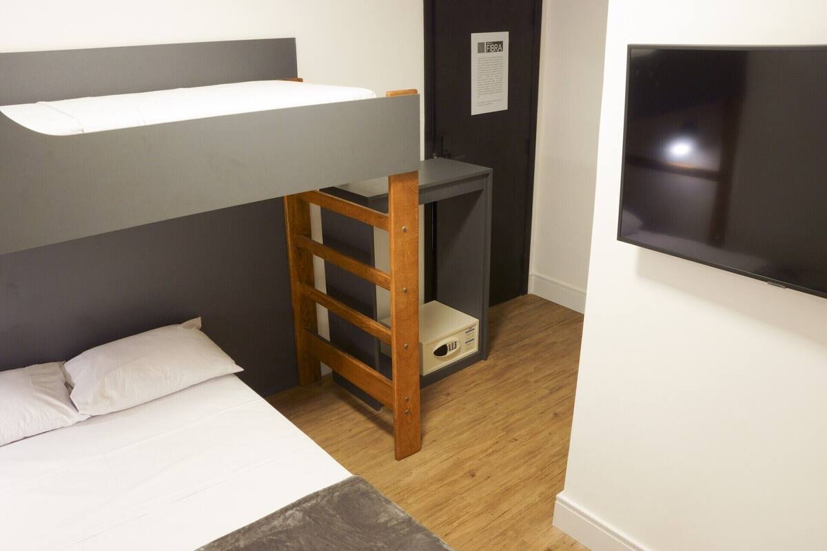 A compact room with a bunk bed, a small desk with a chair, and a TV mounted on the wall.