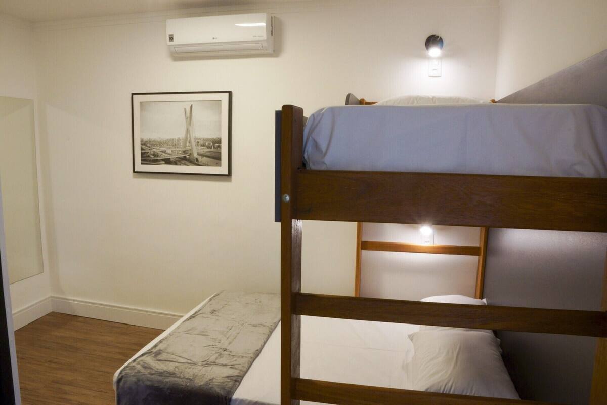 A bunk bed room with a framed picture on the wall, an air conditioner, and a bedside lamp.