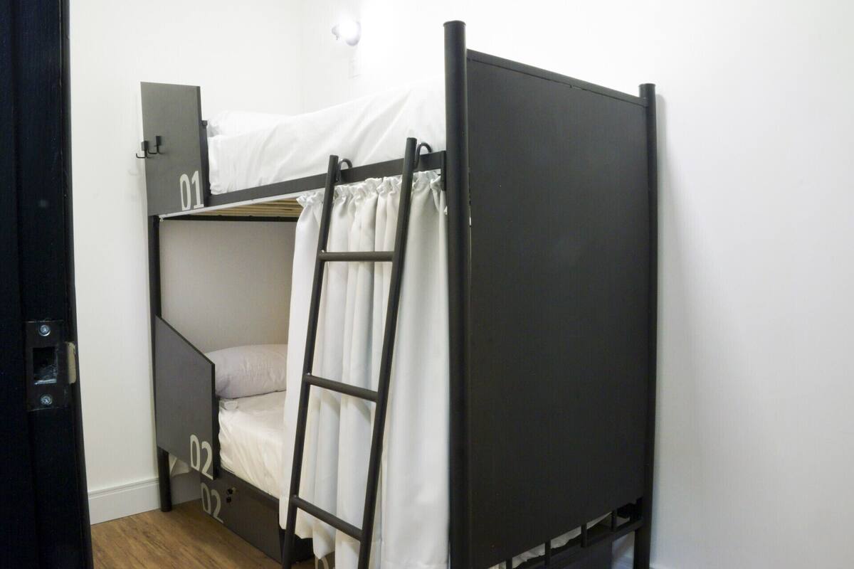 A bunk bed with a ladder, a small desk, and a white curtain.