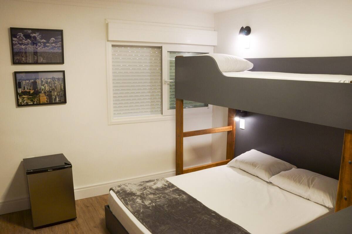 A bunk bed room with a cityscape view, a small fridge, and a window with blinds.