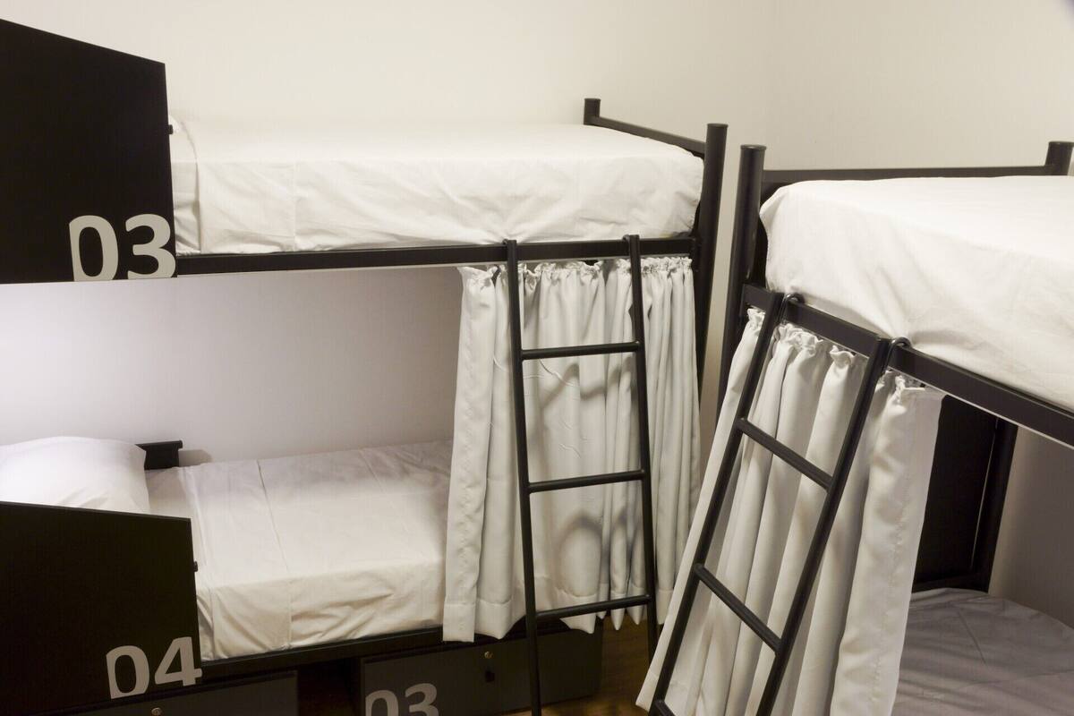 A bunk bed room with three levels, each with a white mattress and black metal frame.
