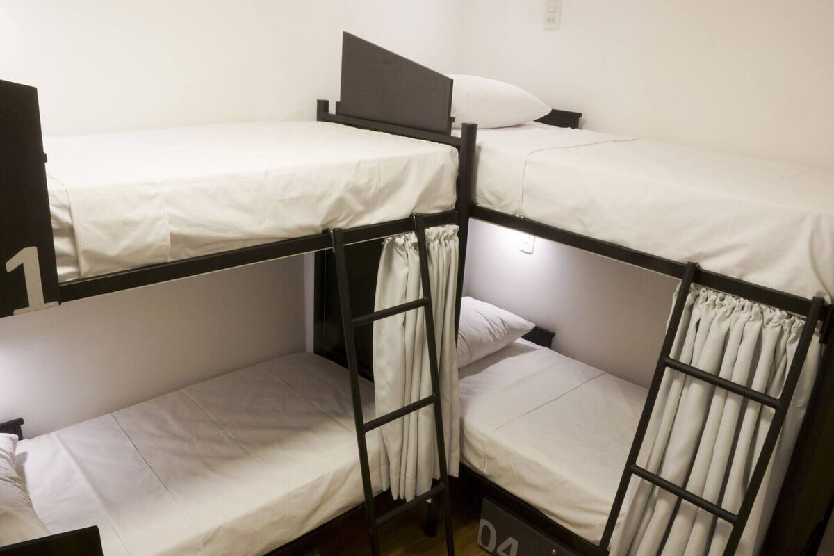 A bunk bed room with three beds, each with a white mattress and black metal frame.