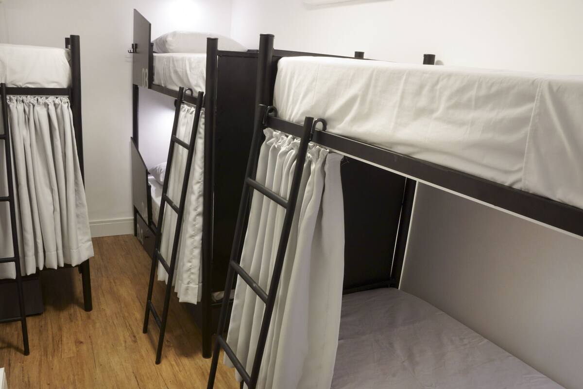 A bunk bed room with a wooden floor, white bedding, and a black metal frame.