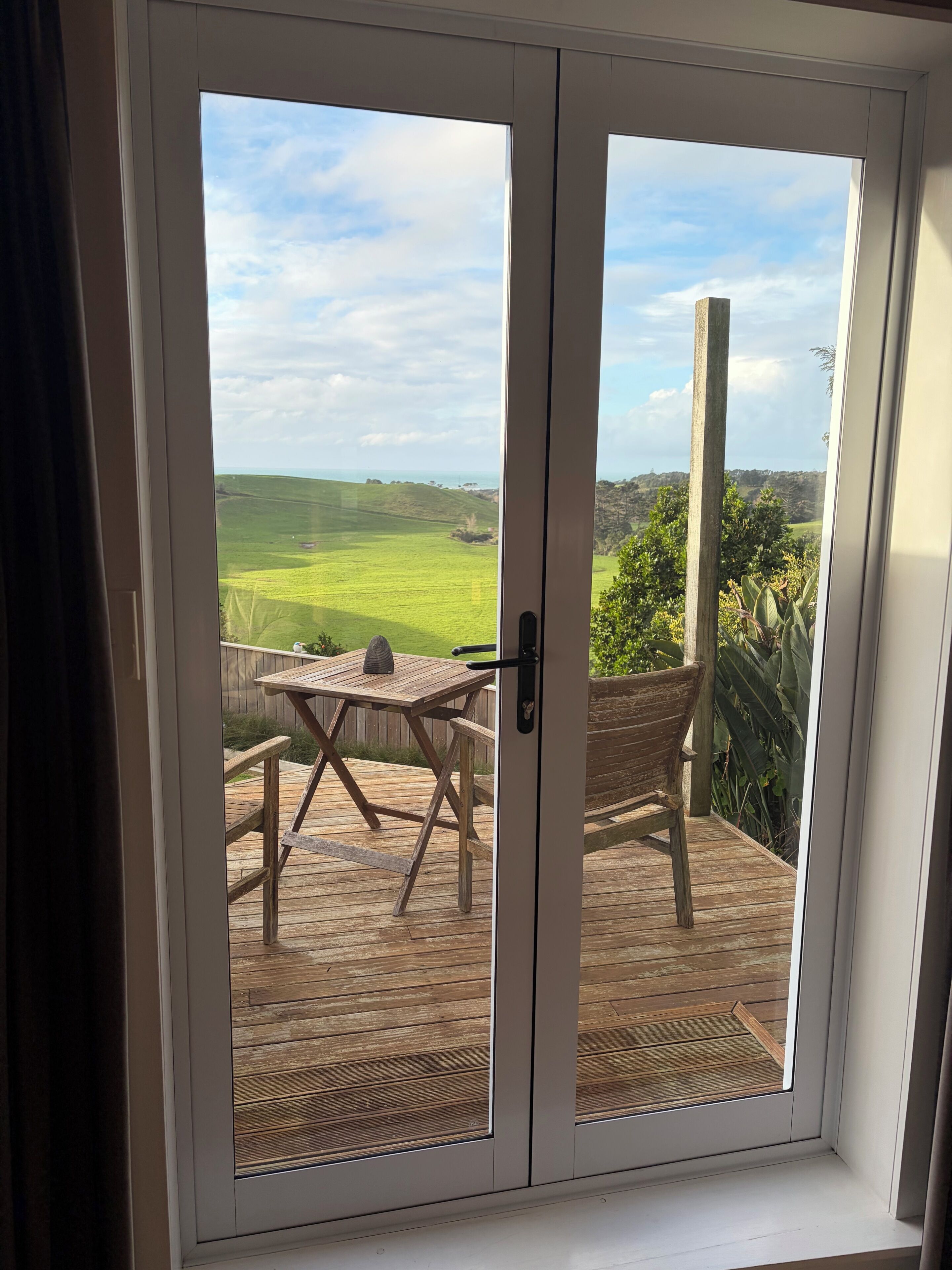 A room with a sliding glass door leading to an outdoor deck with a wooden table and a chair.