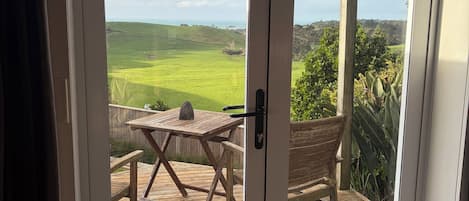 Una habitación con puerta corrediza de vidrio que da a una terraza exterior con mesa y silla de madera.