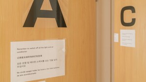 Puerta de madera con letras negras grandes 'A' y 'C' que indican los números de habitación. Un cartel en la puerta indica apagar la luz y el aire acondicionado.