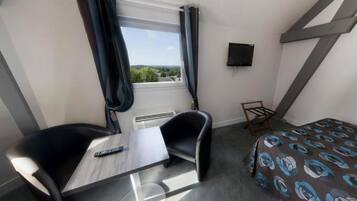 Hotelkamer met een bed, bureau, stoel, televisie en raam met gordijnen.