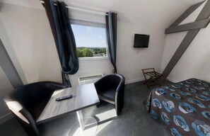 A hotel room with a bed, a desk, a chair, a TV, and a window with curtains. - Hotel De La Tour (Masseret)