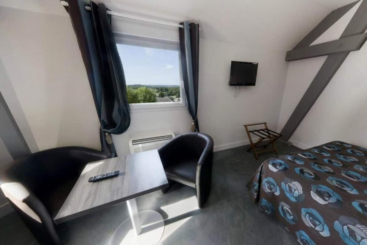 A hotel room with a bed, a desk, a chair, a TV, and a window with curtains.