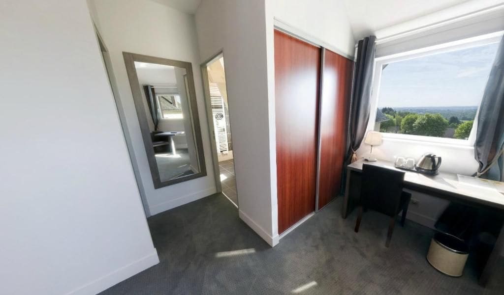 Hotelkamer met een bureau, een stoel, een raam met uitzicht, een kledingkast en een spiegel.