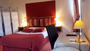 A hotel room with a bed, two bedside tables, a desk with a chair, and a red headboard. - Hotel De La Tour (Masseret)