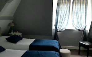 A hotel room with two beds, a chair, a nightstand, and a lamp.