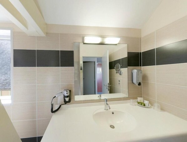 A bathroom with a large mirror, a sink, and a hairdryer on the wall. - Hotel De La Tour (Masseret)