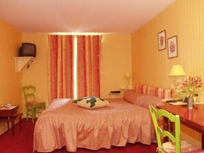 A hotel room with a bed, a desk, a chair, a television, and curtains.