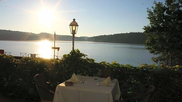 Una mesa lista para comer con vista a un lago y colinas al fondo.