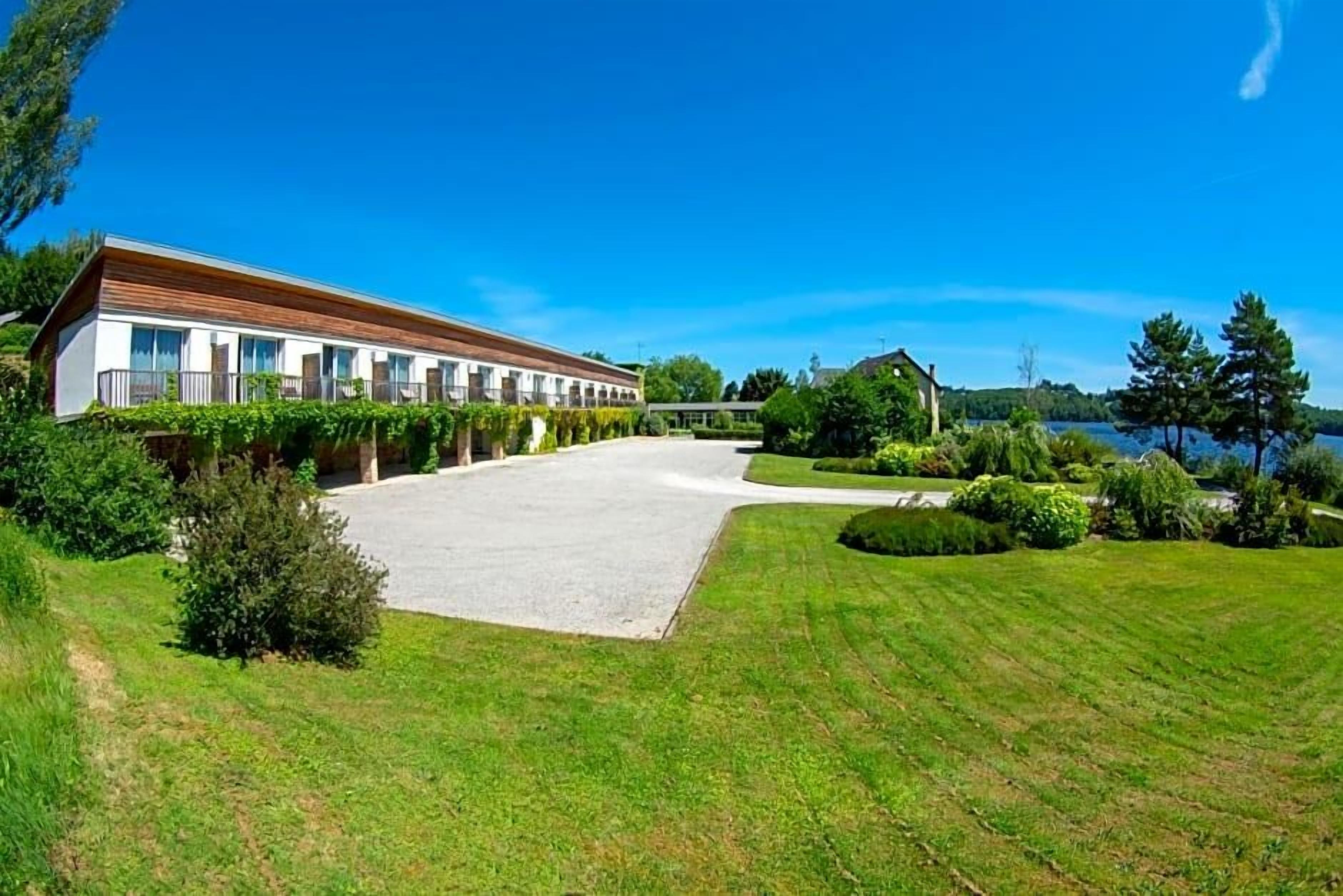 A modern building with a long facade, a paved courtyard, and a lake view.