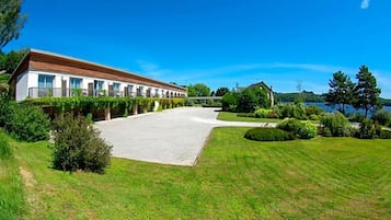 A modern building with a long facade, a paved courtyard, and a lake view.