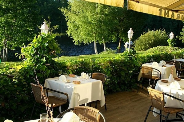 An outdoor dining area with tables set for two, surrounded by lush greenery and trees.
