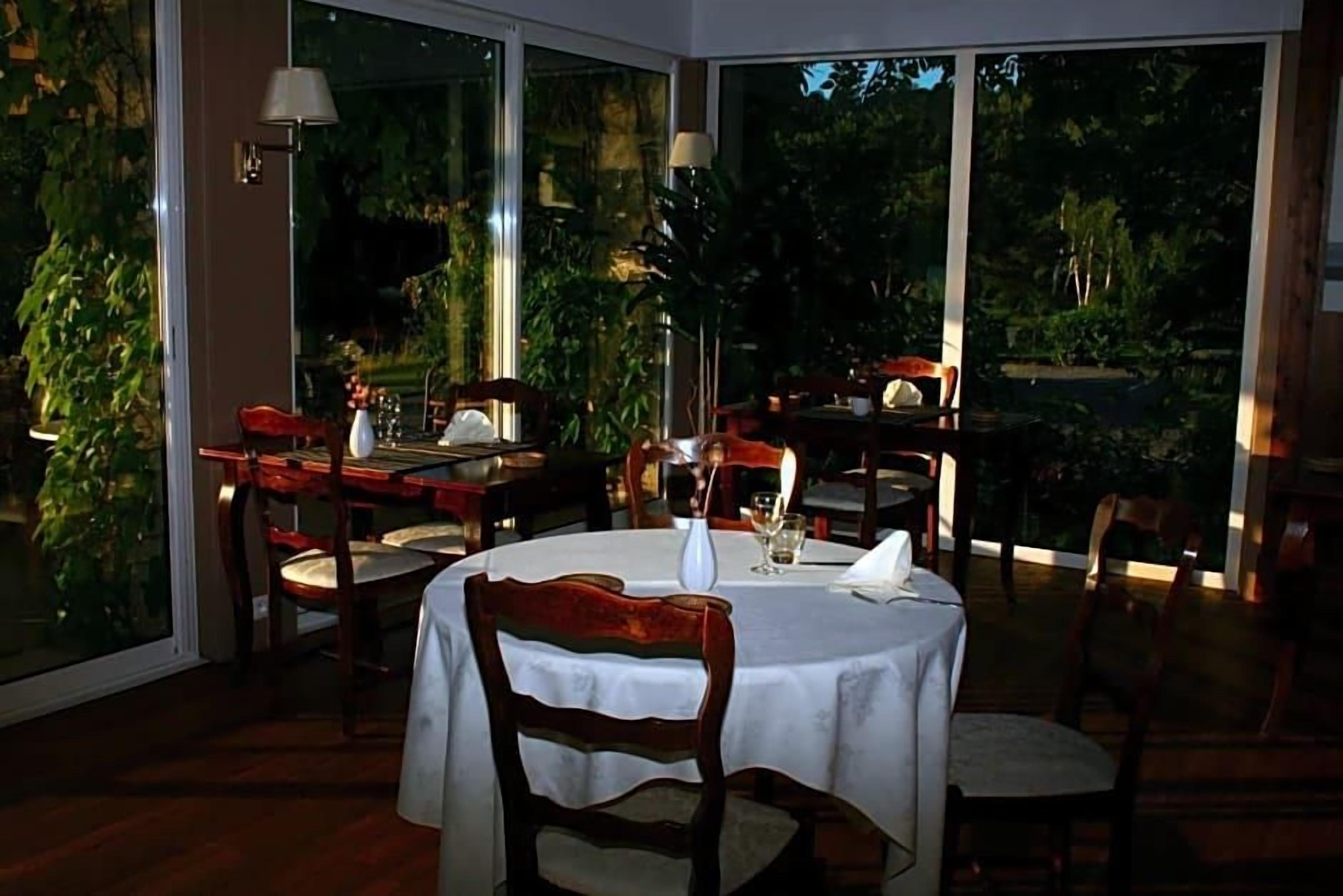 Un comedor con mesas y sillas redondas, ventanas amplias y plantas de interior.