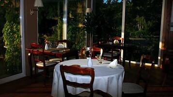 Un comedor con mesas y sillas redondas, ventanas amplias y plantas de interior.