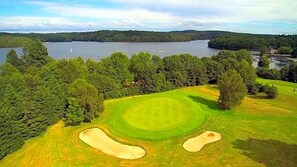 A golf course with a water body in the background, surrounded by dense trees.