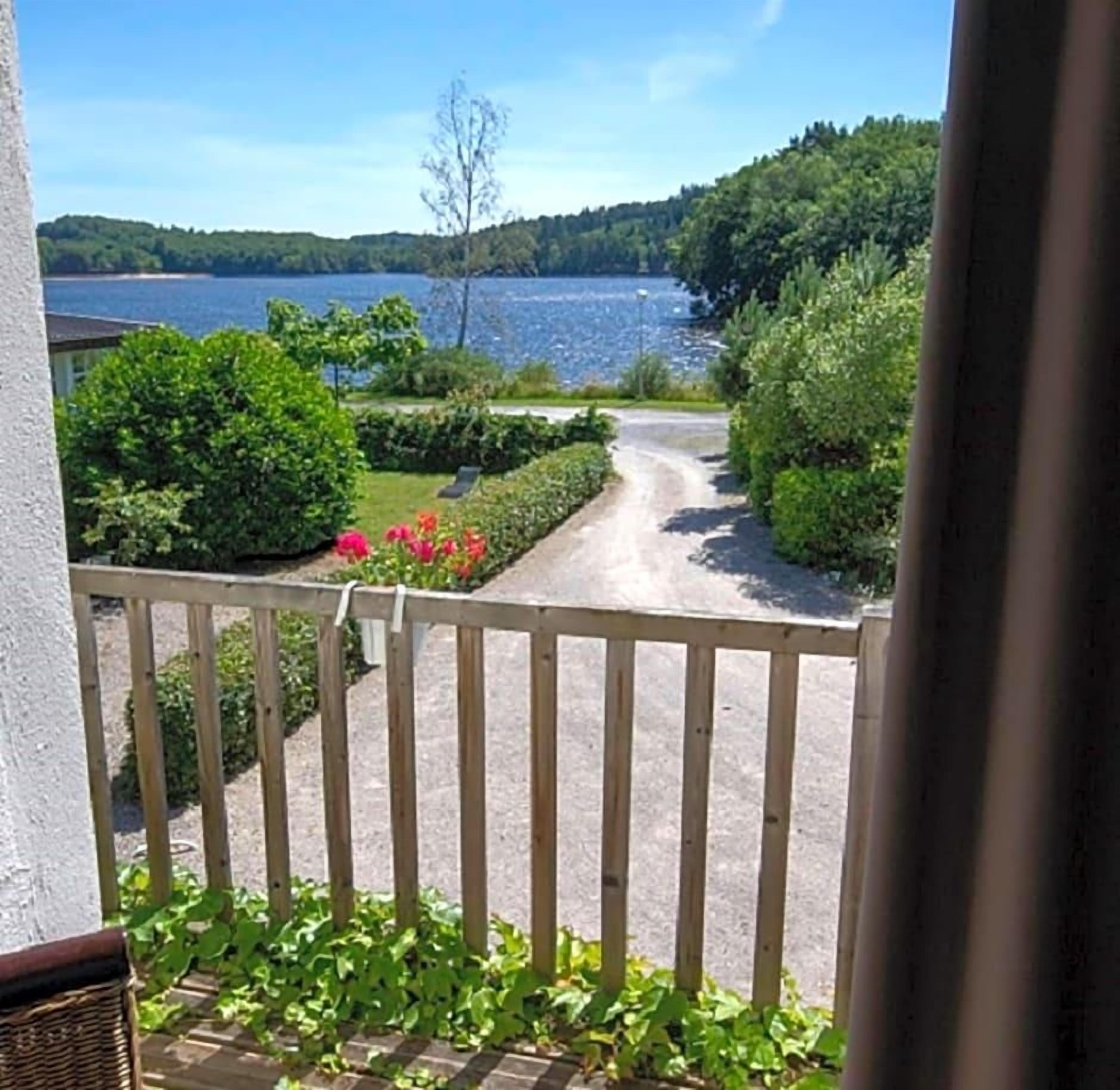 Ein Balkon mit Blick auf einen See, umgeben von Grün und einem Holenzaun.