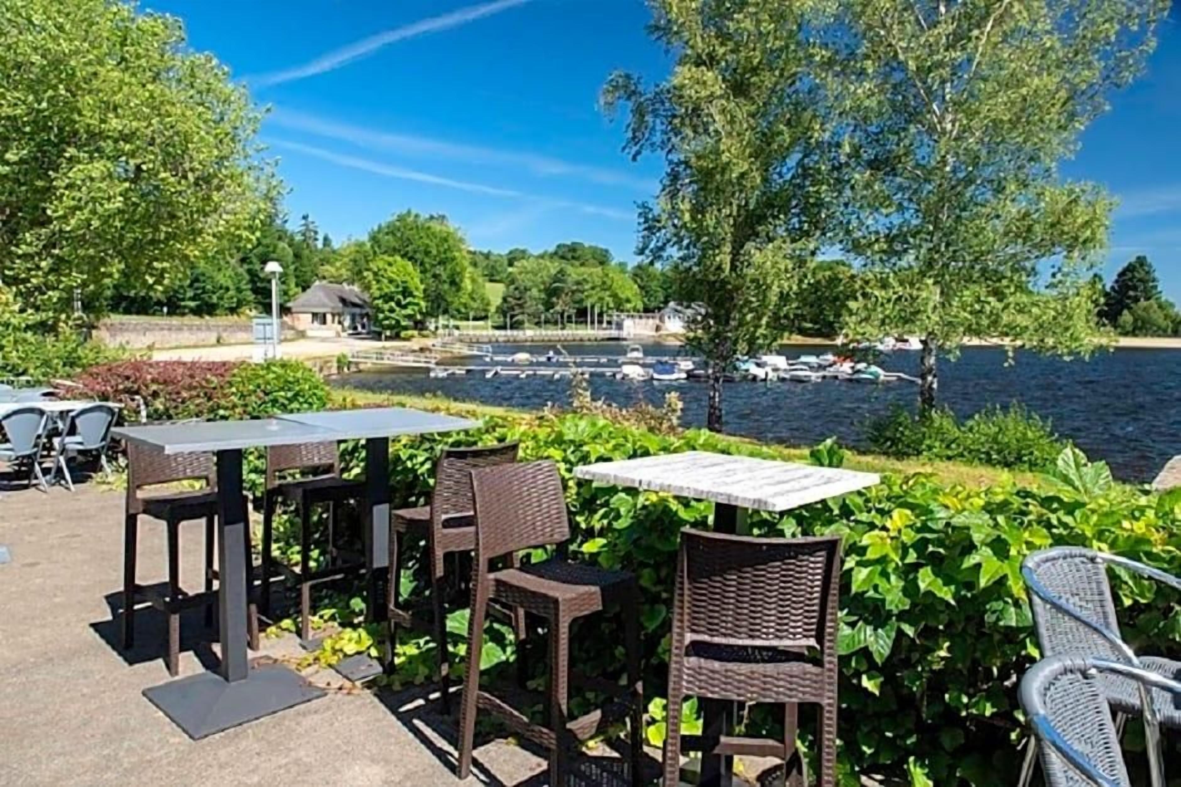 An outdoor seating area with tables and chairs, overlooking a body of water with boats.