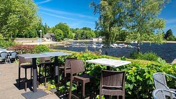 An outdoor seating area with tables and chairs, overlooking a body of water with boats.
