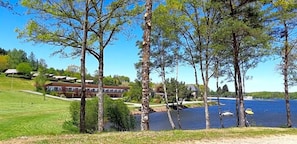 Une propriété située au bord d’un lac, dotée d’une pelouse bien entretenue, de plusieurs arbres et, au fond, d’un bâtiment avec un toit rouge.
